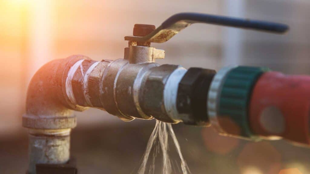 Close-up of a leaking outdoor water pipe with sunlight shining in the background