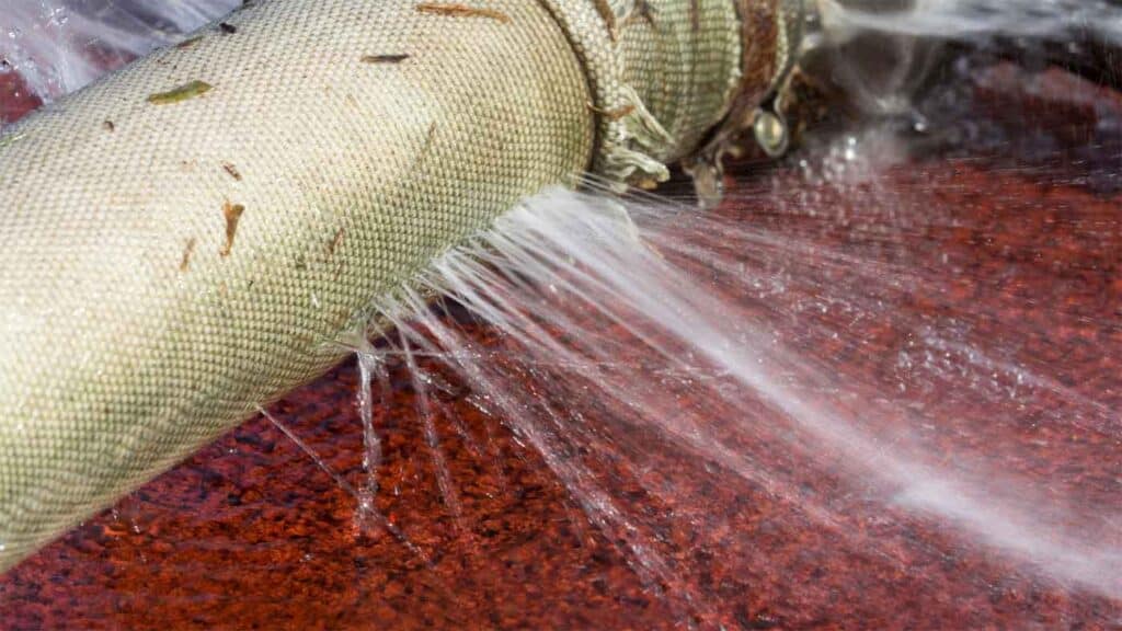 A close-up image of a leaking hose, with water spraying out from multiple holes