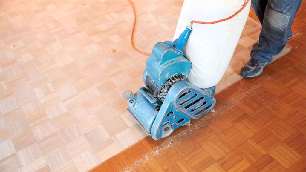 A floor sander in use, refinishing a parquet wood floor with visible progress