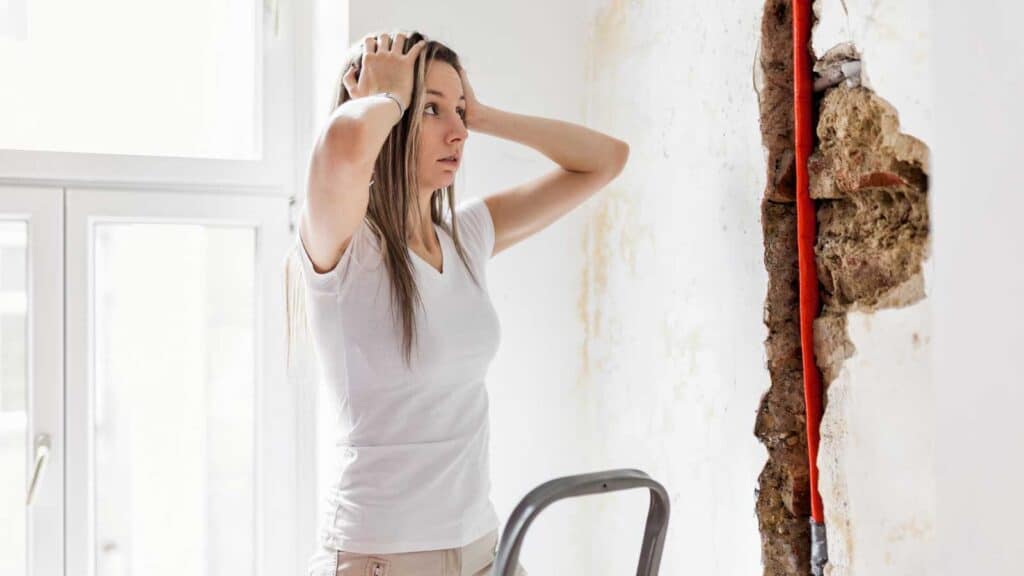 Concerned woman inspecting severe water damage on a wall.