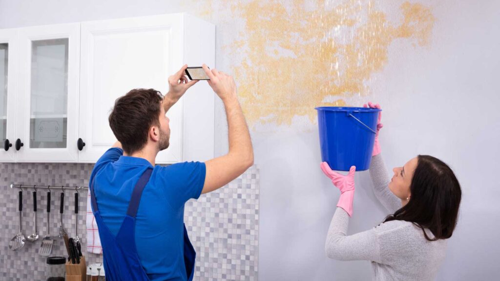 Homeowners capturing water damage while collecting leaks in a bucket.