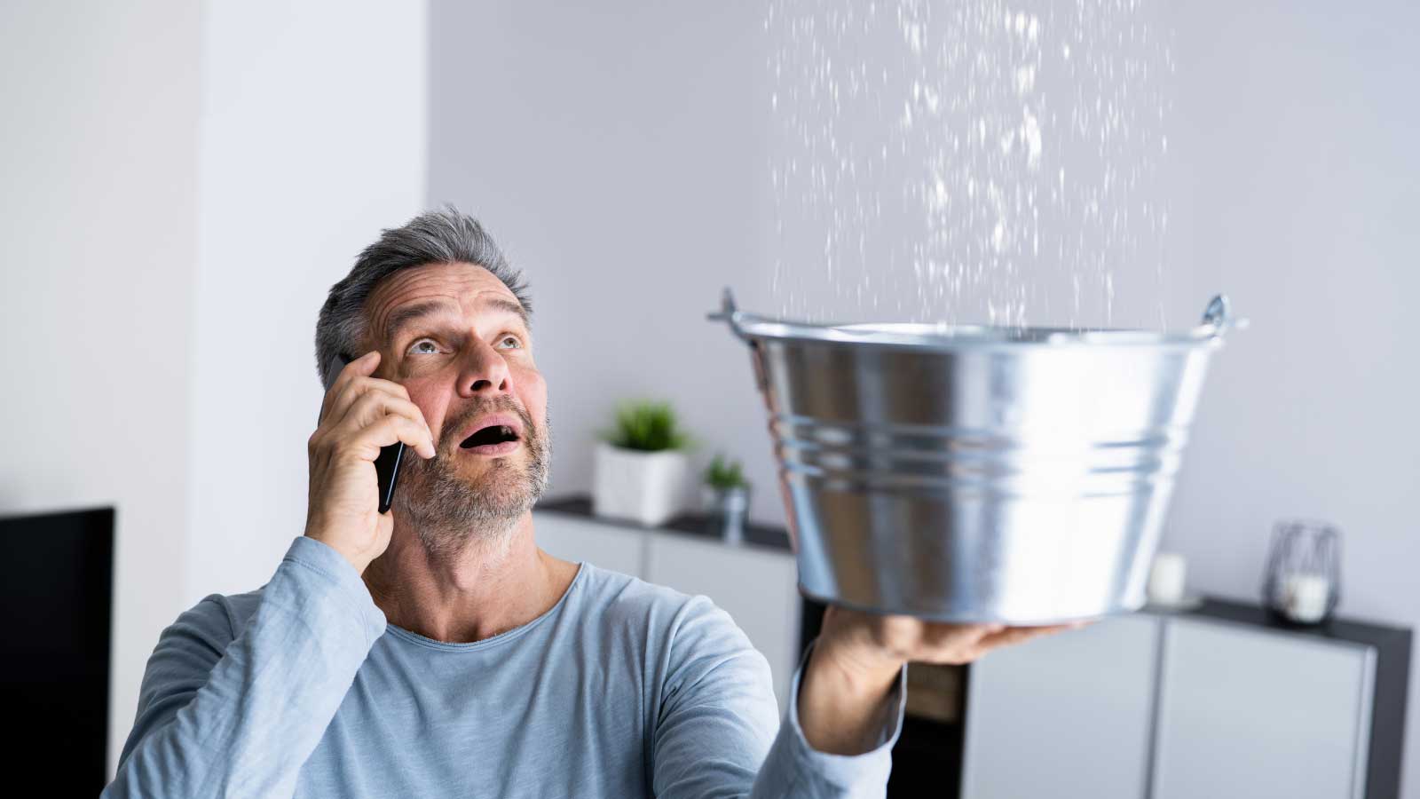 Man holding a bucket to catch water from a ceiling leak