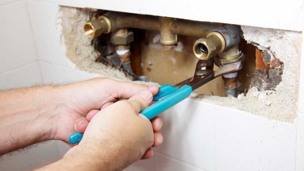  Plumber repairing damaged pipes behind a wall to prevent leaks