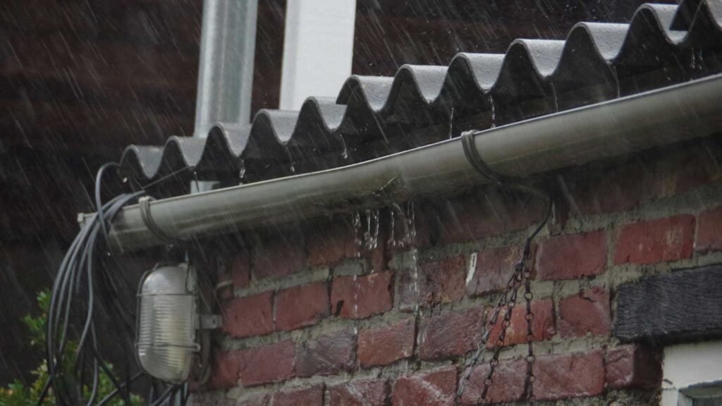 Rainwater overflowing from a clogged gutter on a brick house.