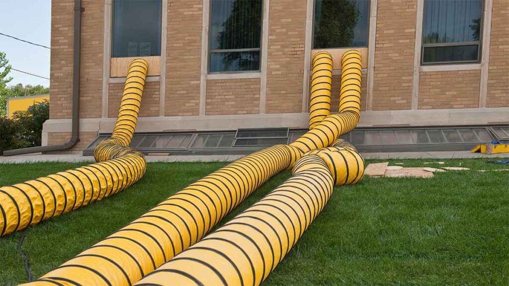 Large drying hoses ventilate a building during water damage restoration.