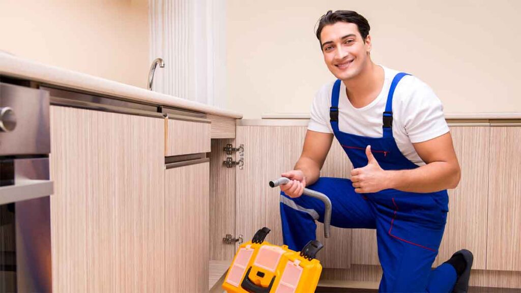  Smiling plumber repairing a kitchen sink with professional equipment.