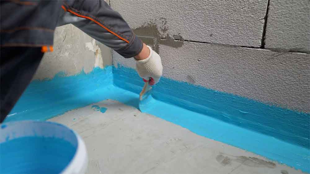 Worker applying blue waterproofing sealant to a concrete wall.