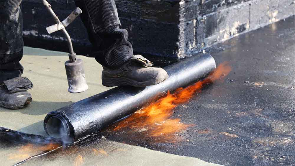 Worker installing a waterproofing membrane using a torch.