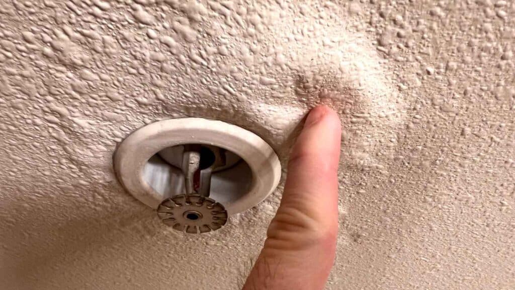  Finger pressing on a water-damaged ceiling near a fire sprinkler head.
