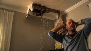 Man reacts to ceiling collapse and heavy water leakage indoors.