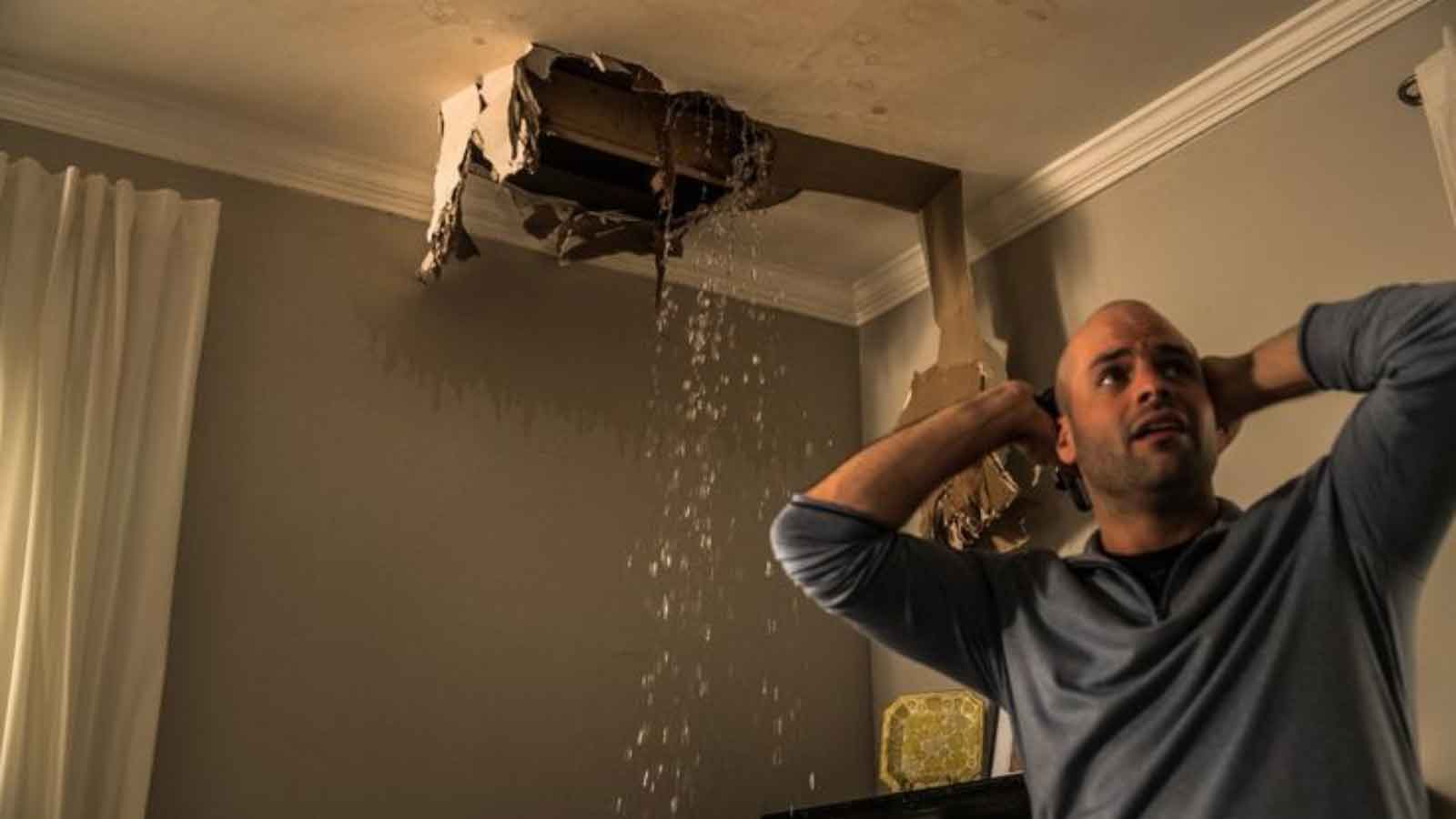 Man reacts to ceiling collapse and heavy water leakage indoors.