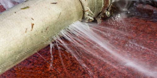 A close-up image of a leaking hose, with water spraying out from multiple holes