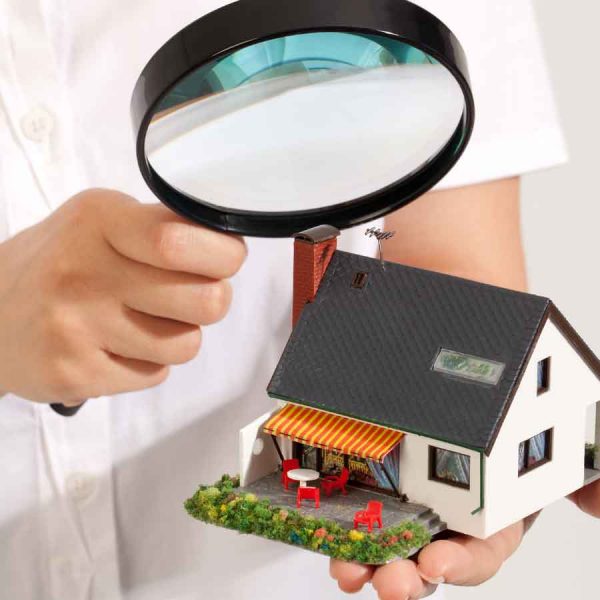 A person examines a model house with a magnifying glass.