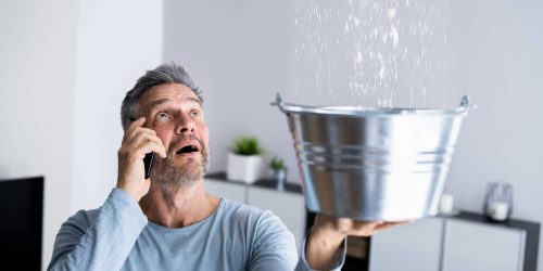 Man holding a bucket to catch water from a ceiling leak