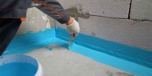 Worker applying blue waterproofing sealant to a concrete wall.